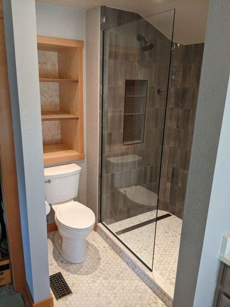 Modern bathroom featuring a glass shower, white toilet, and tiled wall with shelves.