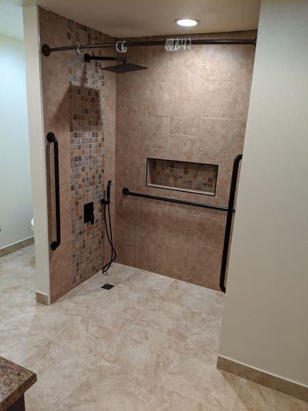 Modern walk-in shower with mosaic tile, grab bars, and overhead showerhead. Accessible design features.