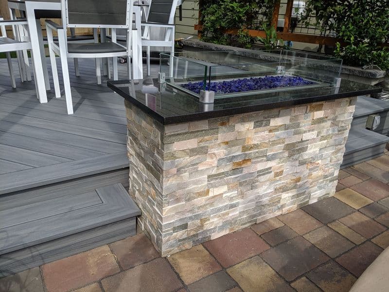 Modern outdoor fire pit with stone base and glass top on a stylish patio deck.