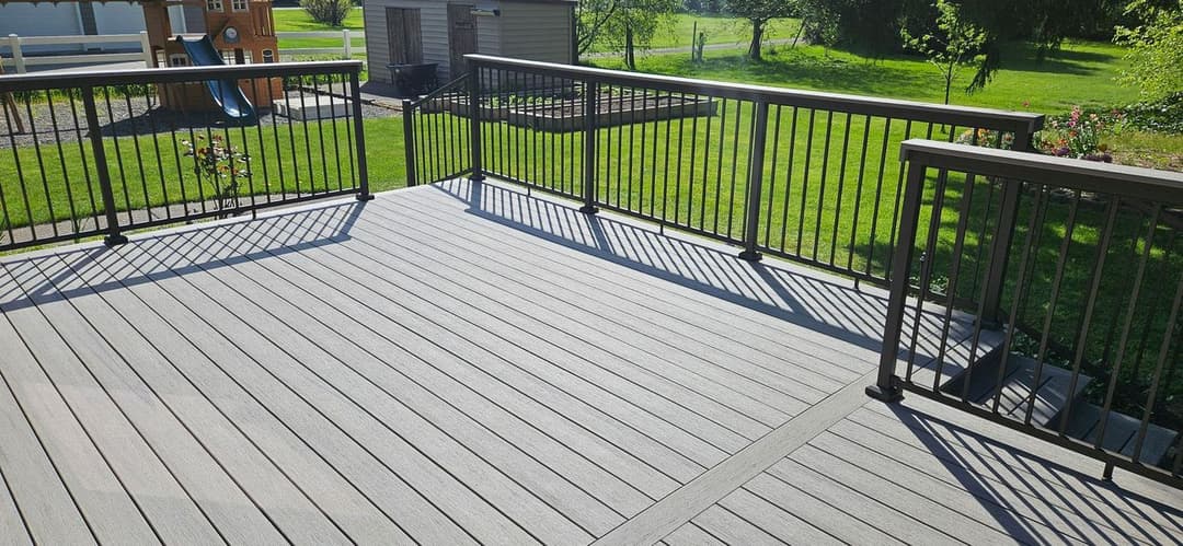 Spacious wooden deck with modern railings overlooking a green yard and play area.
