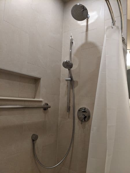 Modern shower with rainfall showerhead, grab bars, and sleek tile design. Accessible bathroom feature.