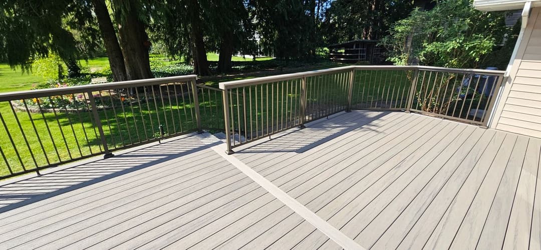 Spacious wooden deck with black railing surrounded by lush green trees and garden.